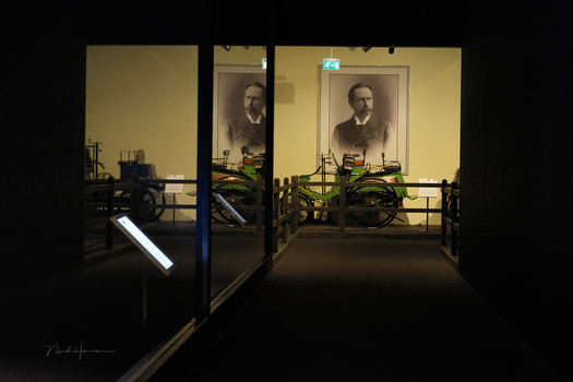 Gallery hallway with symmetrical portrait photographs on illuminated yellow walls and dark floor.
