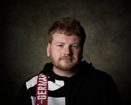 Man wearing black hoodie and red scarf against textured dark background.