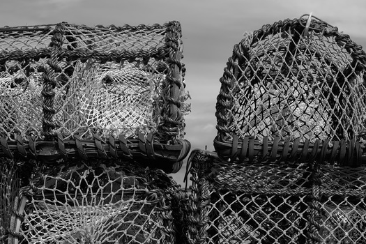Four weathered lobster or crab traps stacked together, photographed in monochrome against an overcast sky.