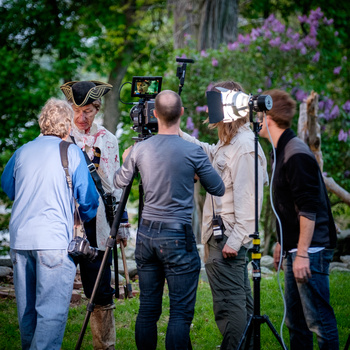Film crew operating professional video cameras during an outdoor production shoot in a garden setting.