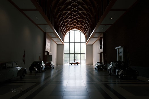 Symmetrical vanishing point shot down a minimalist hallway with dramatic arched wooden ceiling and large window.