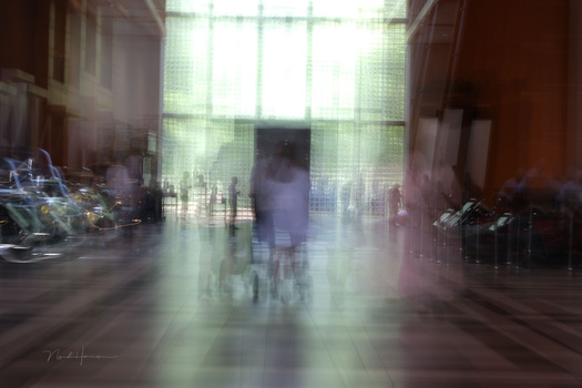Blurred figure walking through a corridor with bright window light and architectural elements on either side.