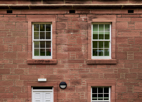 Red brick facade with two multi-pane windows, white door, and dark window below, symmetrically composed.