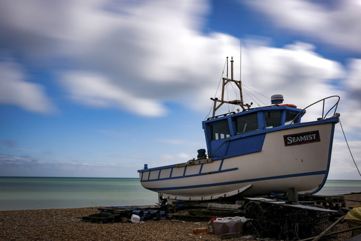 Blue and white fishing vessel named Seamist beached on shingle shore under partly cloudy sky.