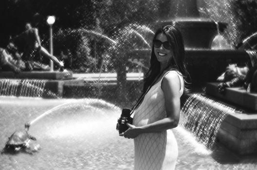 Woman holding a camera in a parking lot, shot in black and white film style.