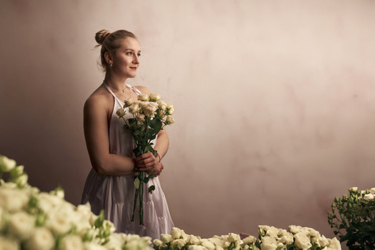 Woman in flowing dress holding white flowers against soft, muted background.