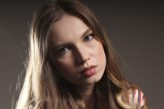 Young woman with long dark hair gazing directly at camera against neutral gray background.