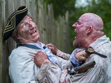 Two men in period costume engaged in a physical struggle against a wooden structure.