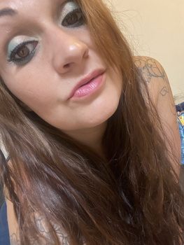 Close-up portrait of a woman with long reddish-brown hair and pink lipstick looking at camera.