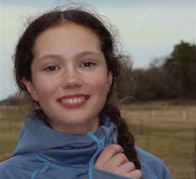 Young woman with long braided hair smiling at camera in outdoor field setting.