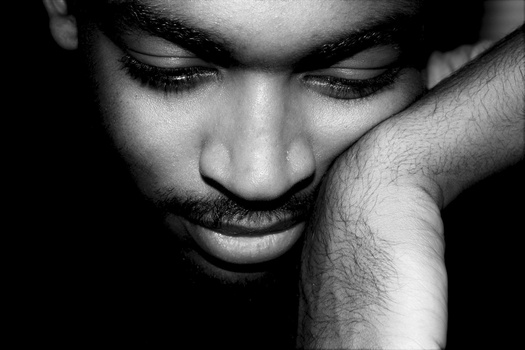 Man with closed eyes and hand resting against face in black and white portrait.