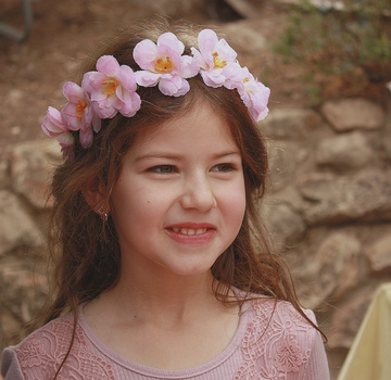 Young girl wearing a pink flower crown and smiling at the camera outdoors.