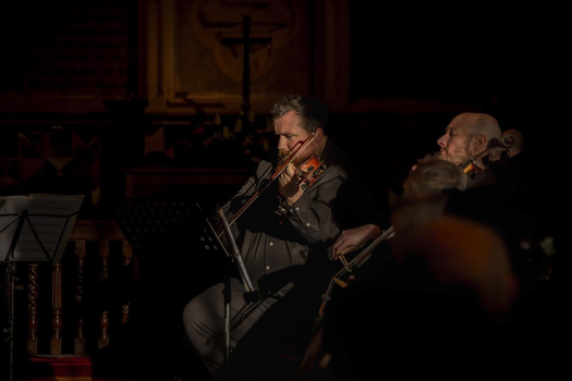 Violinist performing in dramatic stage lighting during an indoor concert.