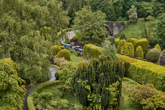 Aerial view of a formal garden with manicured hedges, cypress trees, and winding pathways.
