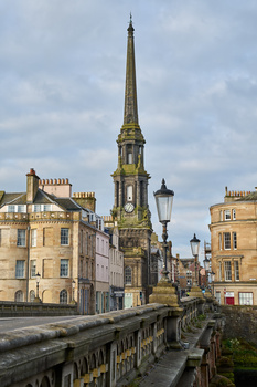 Historic stone church with tall golden spire dominates a European street lined with period buildings.