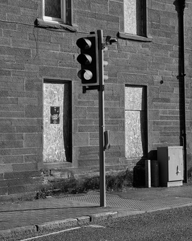 Traffic light mounted on pole against brick building facade in black and white.