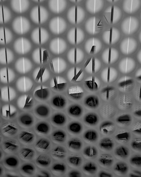 High-contrast black and white photograph of hanging utensils and objects suspended against a textured grid background.