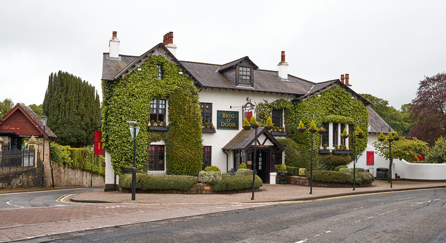 Traditional English pub with ivy-covered white and dark timber-framed walls, featuring dormer windows and chimneys, positioned at a street corner.