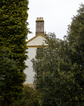 Ivy-covered trees frame a distant stone house with a tall chimney and pitched roof.