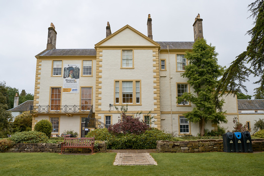 Georgian-style stone manor house with cream-colored facade, multiple chimneys, and ivy-covered walls, fronted by manicured lawn.