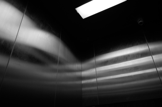 Interior of a modern elevator with brushed metal walls and recessed ceiling lights creating dramatic linear shadows.