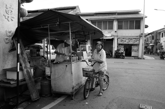 Street vendor with bicycle cart in urban marketplace, black and white photograph.