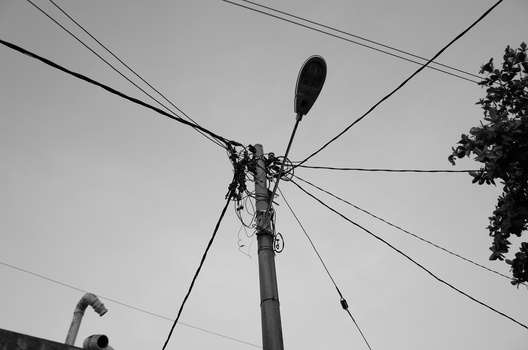 Utility pole with street lamp and multiple power lines converging at the top against an overcast sky.