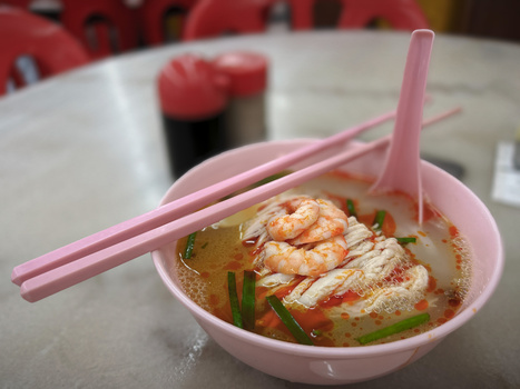 Bowl of Asian noodle soup with shrimp, topped with green onions and served with pink chopsticks.