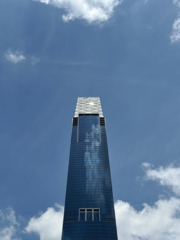 Modern skyscraper photographed from directly below against blue sky with white clouds.