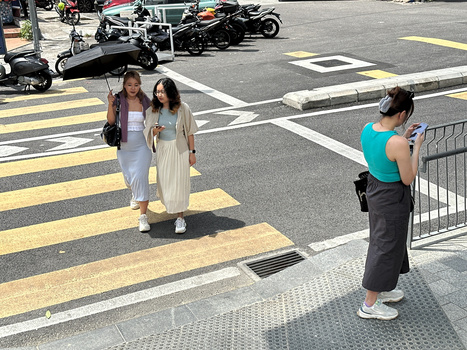 Photographer in turquoise shirt taking a portrait of two women on a zebra crossing during daytime.
