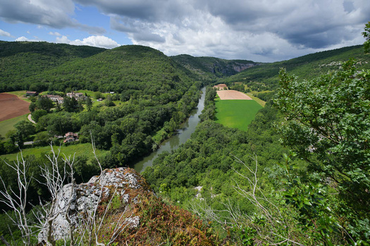 River valley landscape with forested hills, agricultural fields, and a rocky outcrop in the foreground.
