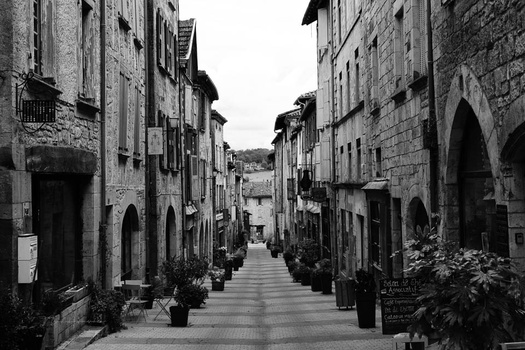 Narrow European cobblestone street lined with historic stone buildings in black and white.