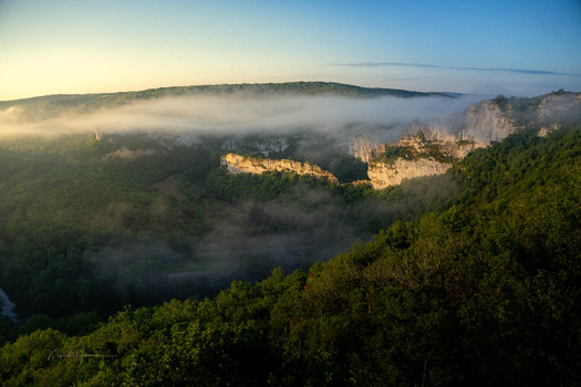 Misty valley with forested cliffs illuminated by golden morning light.