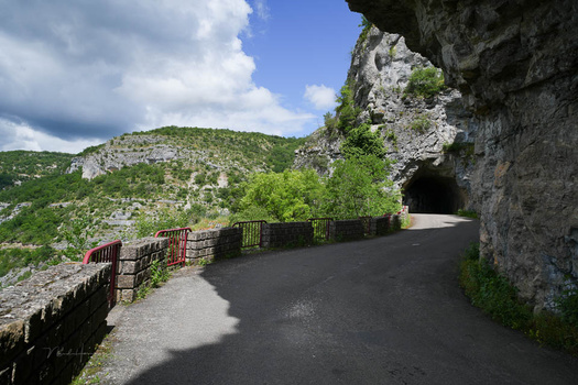Road passing through a limestone cave tunnel with a wooden railing, green hillside visible beyond the opening.