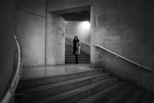 Woman standing on stairs in a concrete underground passage, backlit by natural light from above.
