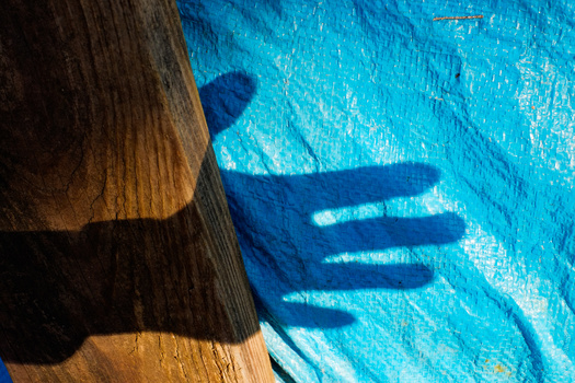Shadow of a hand reaching into bright blue water alongside weathered wooden edge.