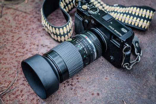 Vintage rangefinder camera with telephoto lens and woven fabric camera strap on textured surface.