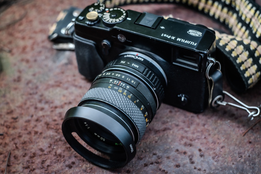 Black rangefinder film camera with manual focus lens on textured fabric background.
