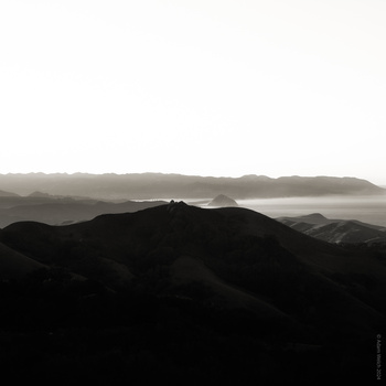 Silhouetted mountain ridges layered in atmospheric haze beneath a misty sky.