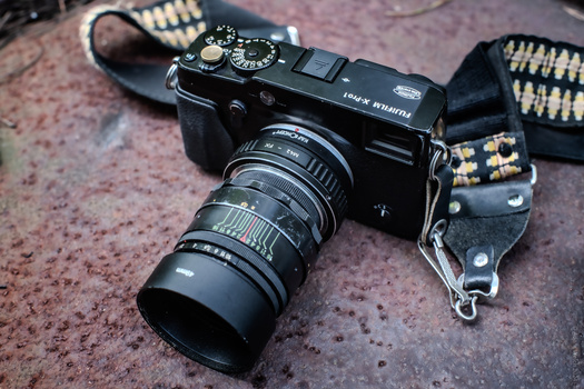 Vintage rangefinder camera with telephoto lens mounted on studded leather camera strap.