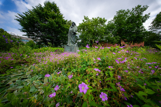 White stone statue surrounded by vibrant magenta flowers in a lush garden setting.