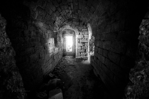 Stone archway tunnel with bright light source visible at the far end, creating strong contrast against dark interior walls.