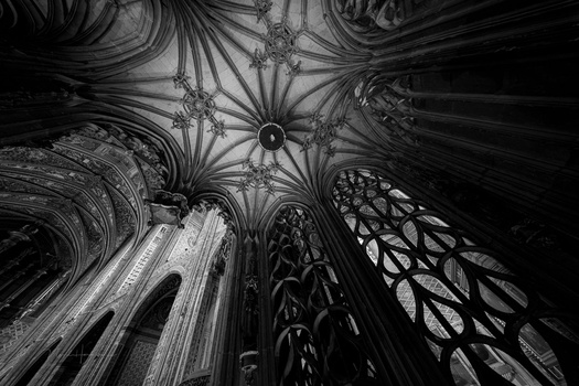 Gothic cathedral ceiling with ribbed vaults and rose window, shot from directly below in black and white.