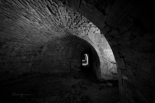 Dark stone tunnel with arched ceiling and distant light visible through opening.