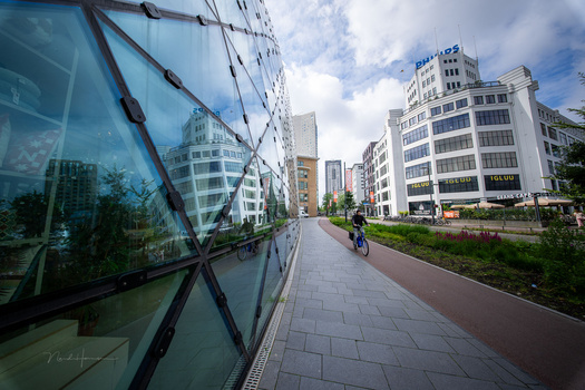 Urban pedestrian pathway lined with modern apartment buildings and reflective glass facade on left side.