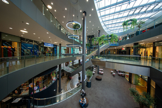 Modern multi-level shopping mall interior with skylights, escalators, and retail storefronts across three visible floors.
