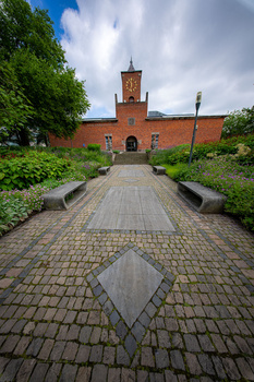 Symmetrical brick pathway leading toward a red brick building with a clock tower under dramatic cloudy skies.