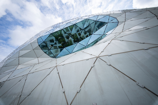 Modern curved building facade with white ribbed cladding and a large oval glass window.