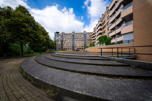 Modern residential complex with curved concrete pathways and apartment buildings under blue sky.