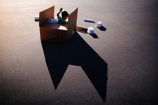 Creative composite showing a person in a cardboard box casting a large shadow shaped like an elephant on a textured floor.